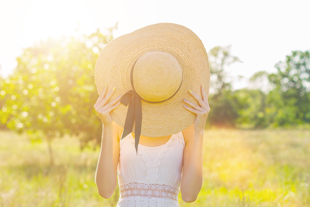 Woman with hat hiding her face in sunny field